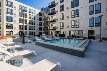 A pool with lounge chairs in front of an apartment building
